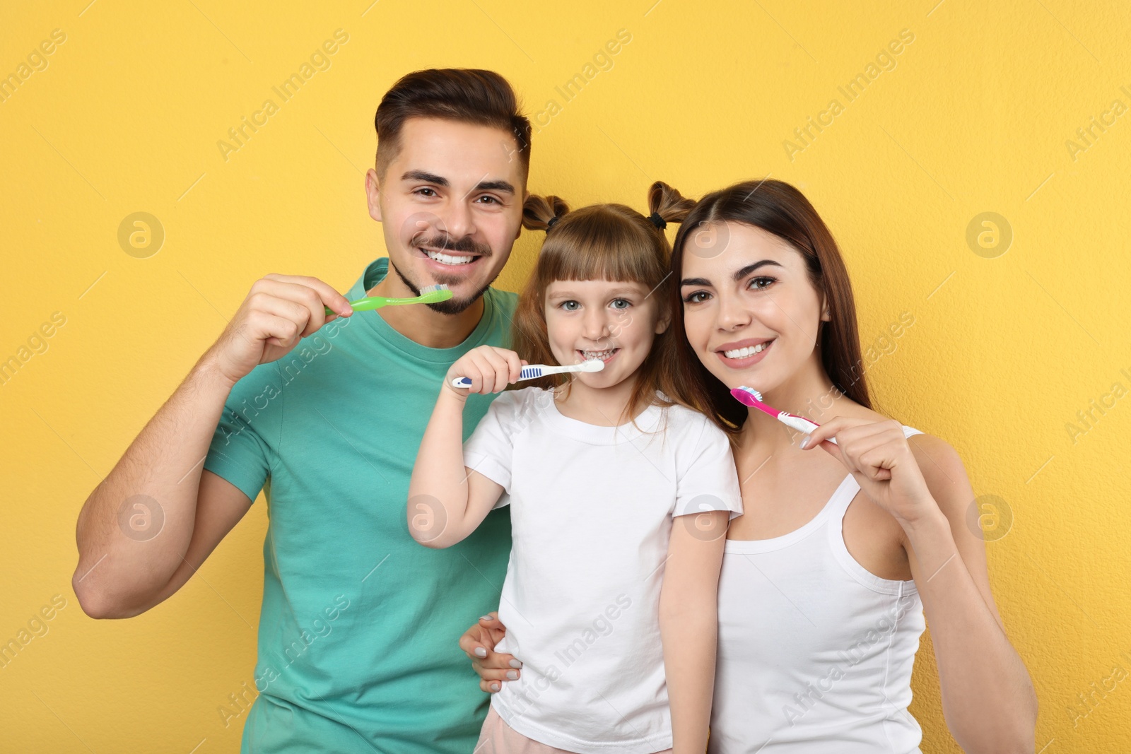 Photo of Little girl and her parents brushing teeth together on color background