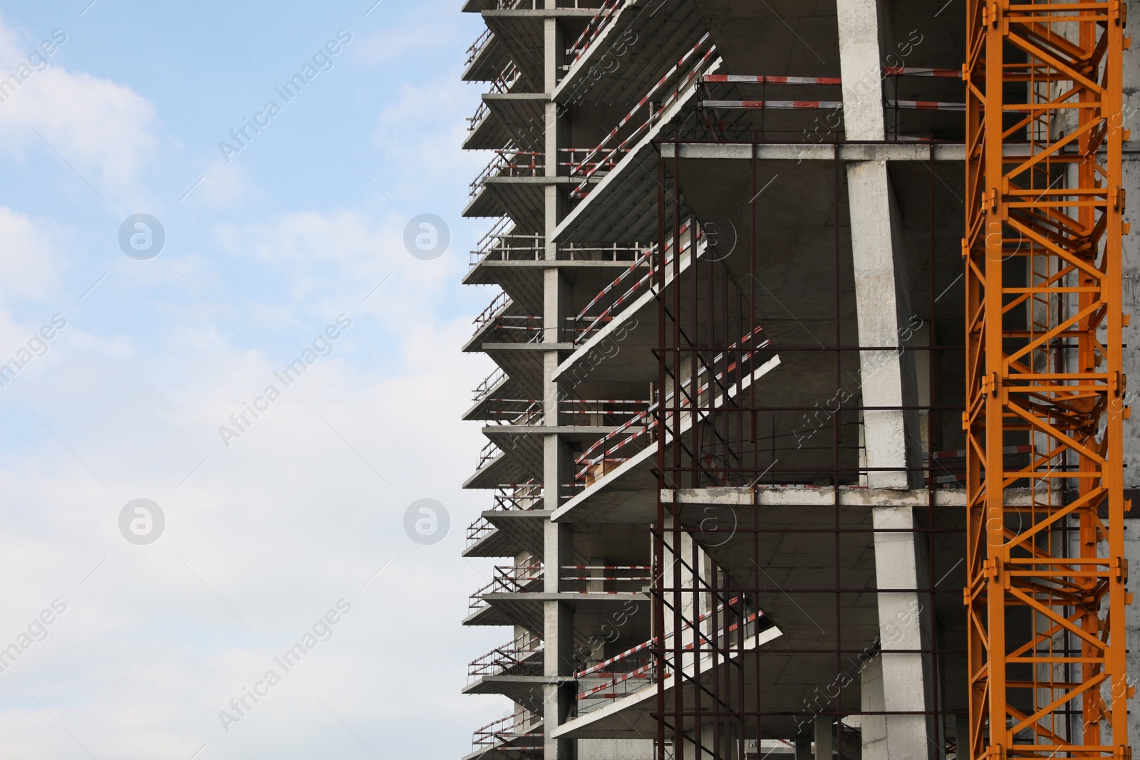 Photo of Construction site with tower crane near unfinished building under cloudy sky. Space for text