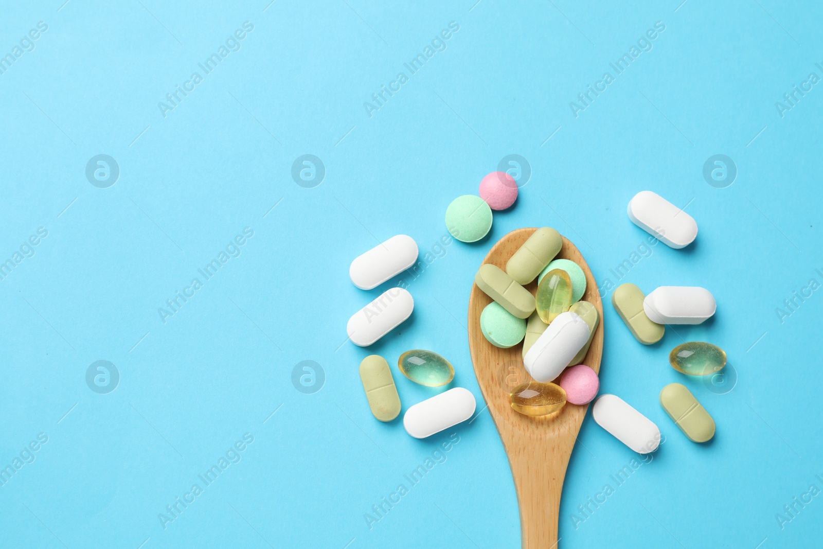 Photo of Different vitamin pills in wooden spoon on light blue background, top view. Space for text