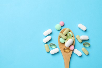 Photo of Different vitamin pills in wooden spoon on light blue background, top view. Space for text