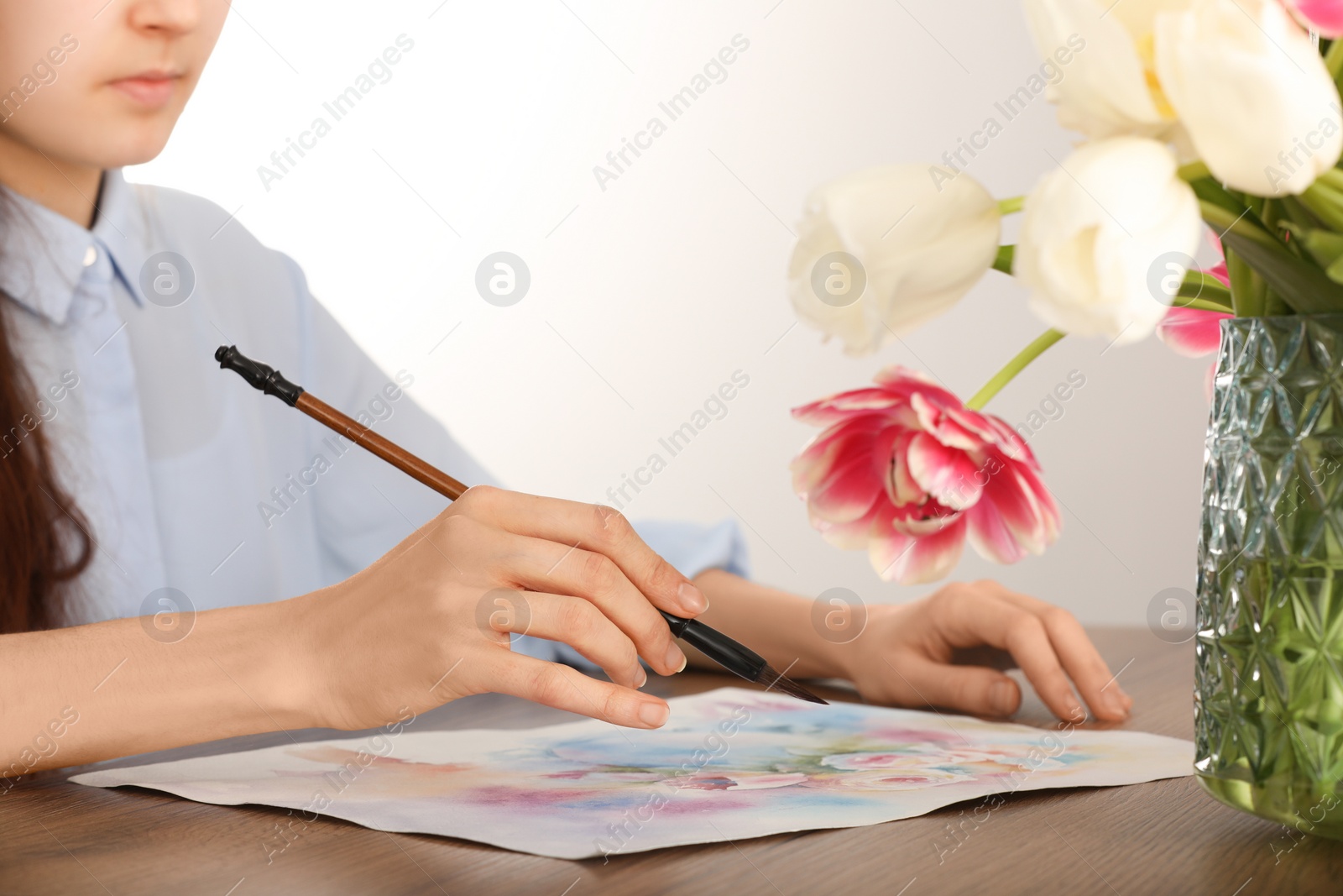 Photo of Woman painting flowers with watercolor at wooden table indoors, closeup. Creative artwork