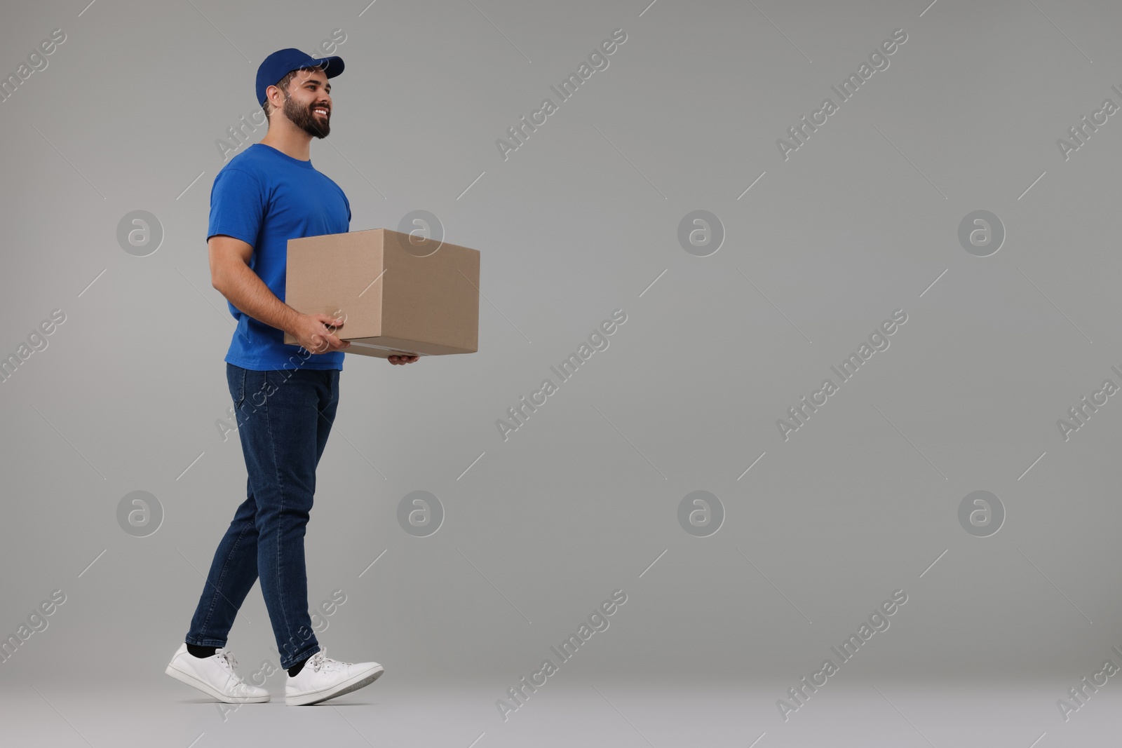 Photo of Happy young courier with parcel on grey background, space for text