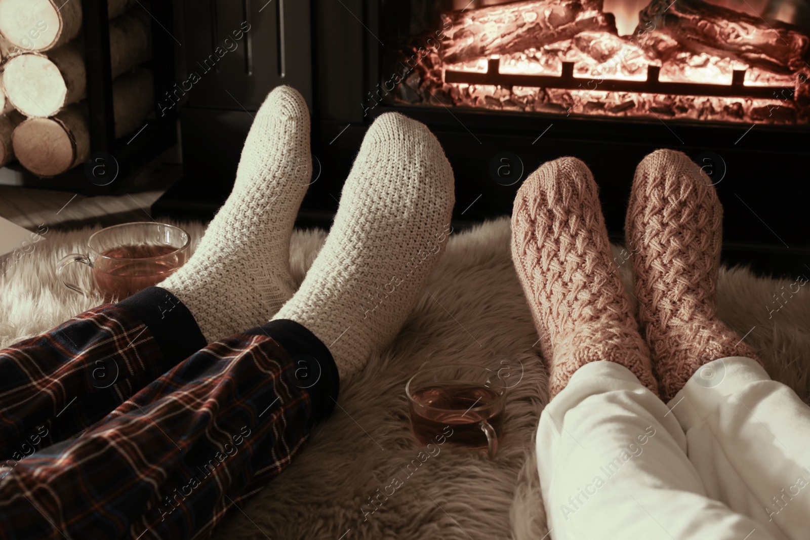 Photo of Couple in knitted socks near fireplace at home, closeup of legs