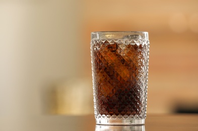 Glass of cola with ice on table against blurred background