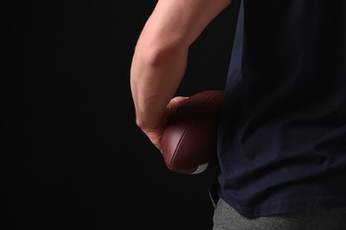 Photo of Athletic man with American football ball on black background, closeup. Space for text