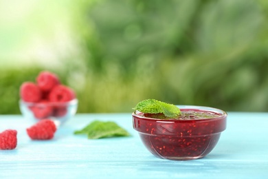 Bowl with raspberry jam on table against blurred background