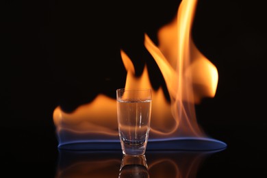 Photo of Vodka in shot glass and flame on black background