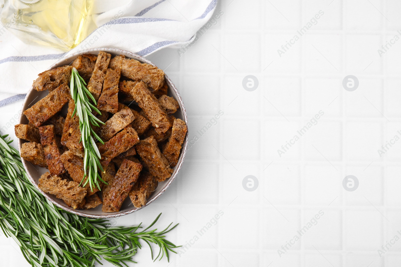 Photo of Crispy rusks with rosemary on white tiled table, flat lay. Space for text