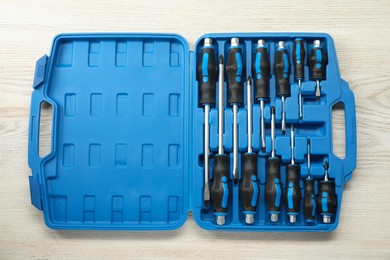 Set of screwdrivers in open toolbox on light wooden table, top view