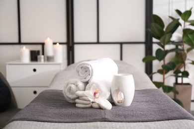 Photo of Towels, aroma lamp, orchid flower and stones on couch in spa salon