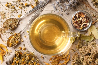Photo of Glass cup of aromatic freshly brewed tea near different dry herbs on wooden table, flat lay