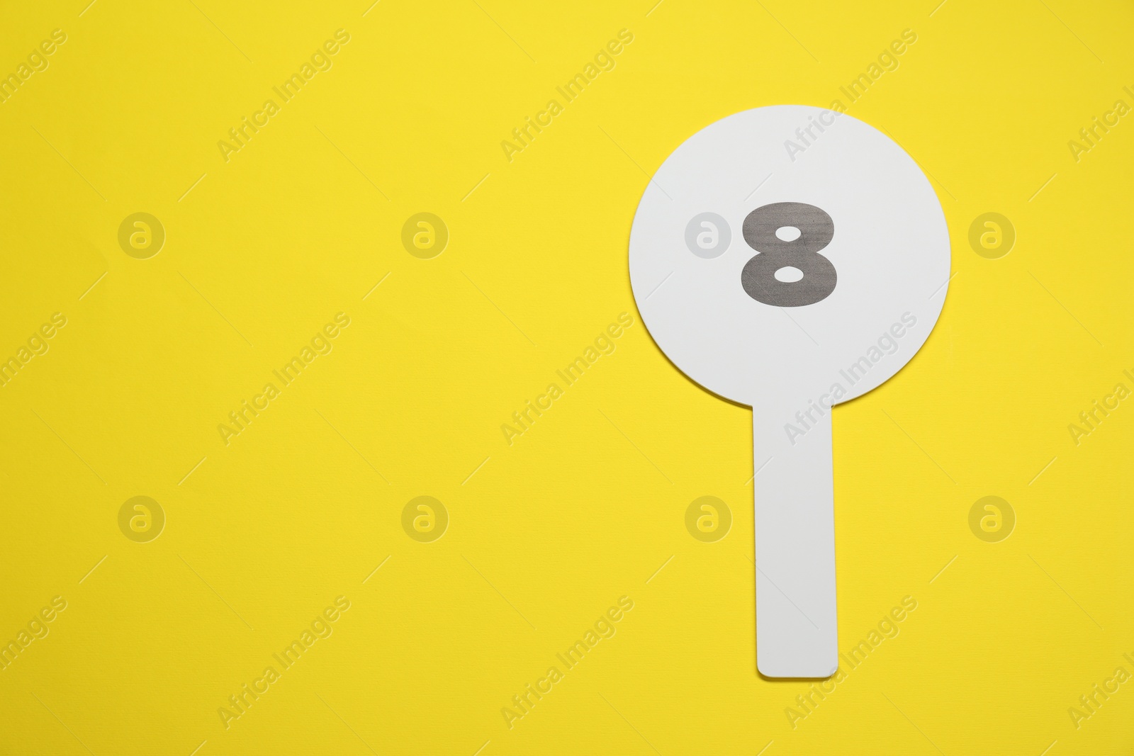 Photo of Auction paddle with number 8 on yellow background, top view. Space for text