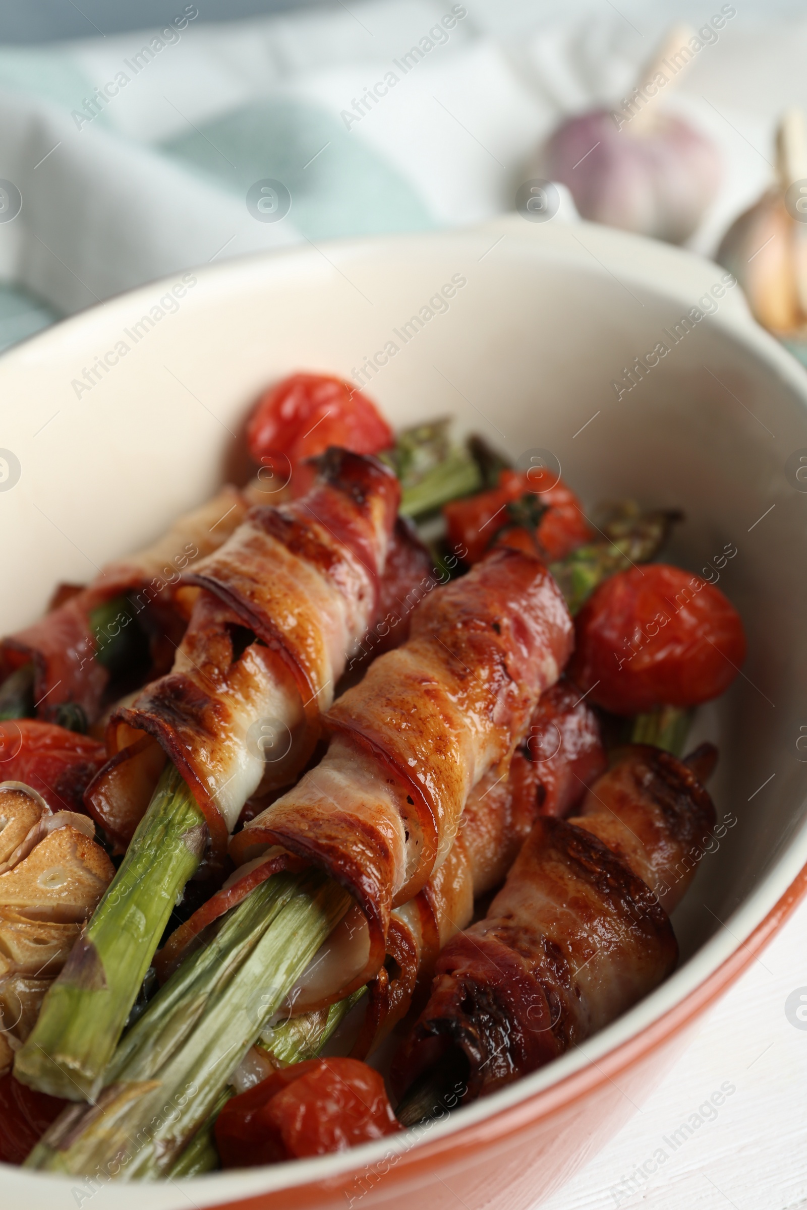 Photo of Oven baked asparagus wrapped with bacon in ceramic dish on white table, closeup