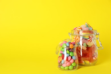 Photo of Jars with different delicious candies on yellow background. Space for text