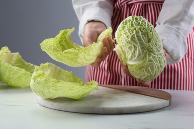 Photo of Woman separating leaf from fresh savoy cabbage at white marble table, closeup