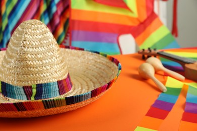 Photo of Mexican sombrero hat on orange table, closeup. Space for text