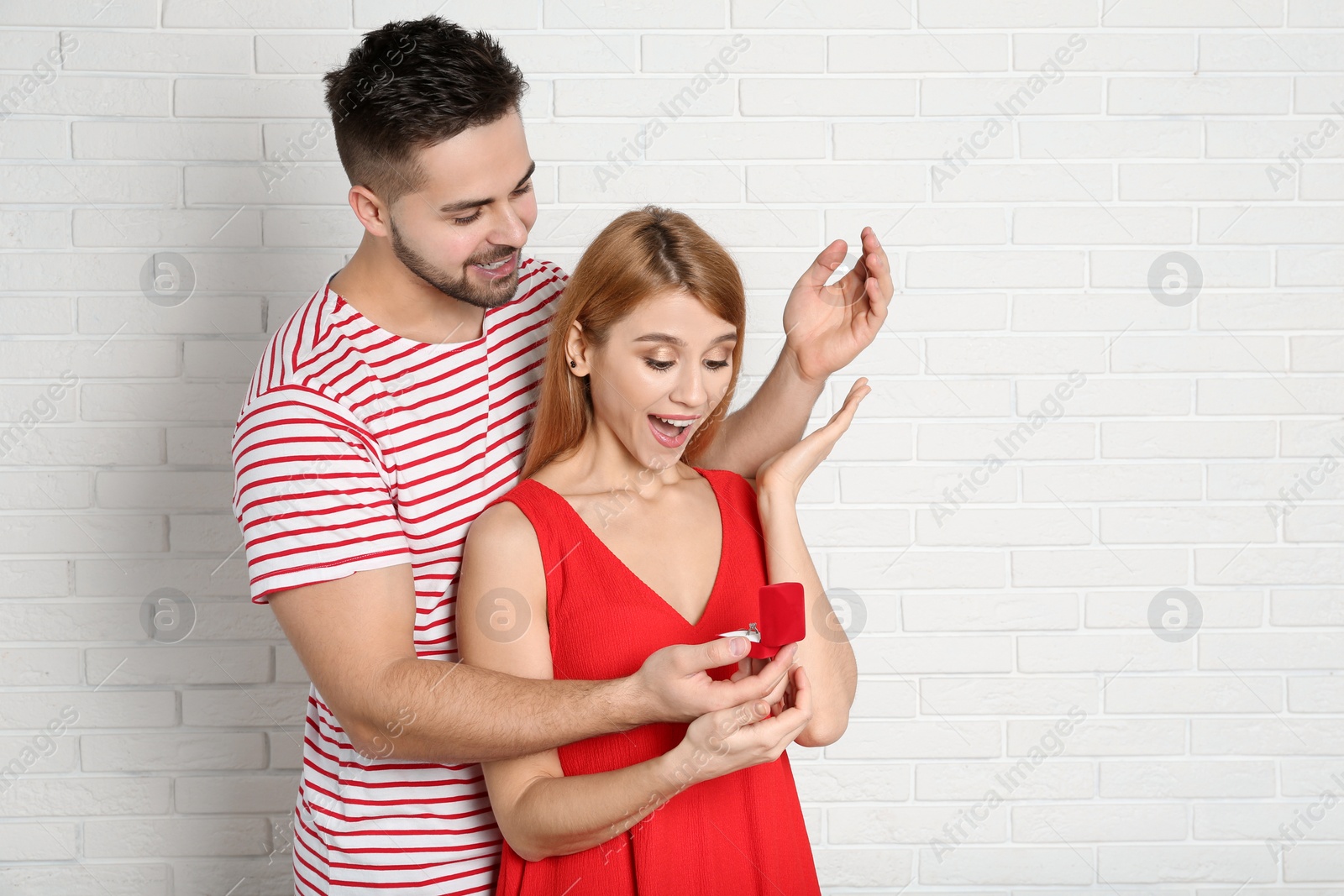 Photo of Man with engagement ring making marriage proposal to girlfriend near white brick wall