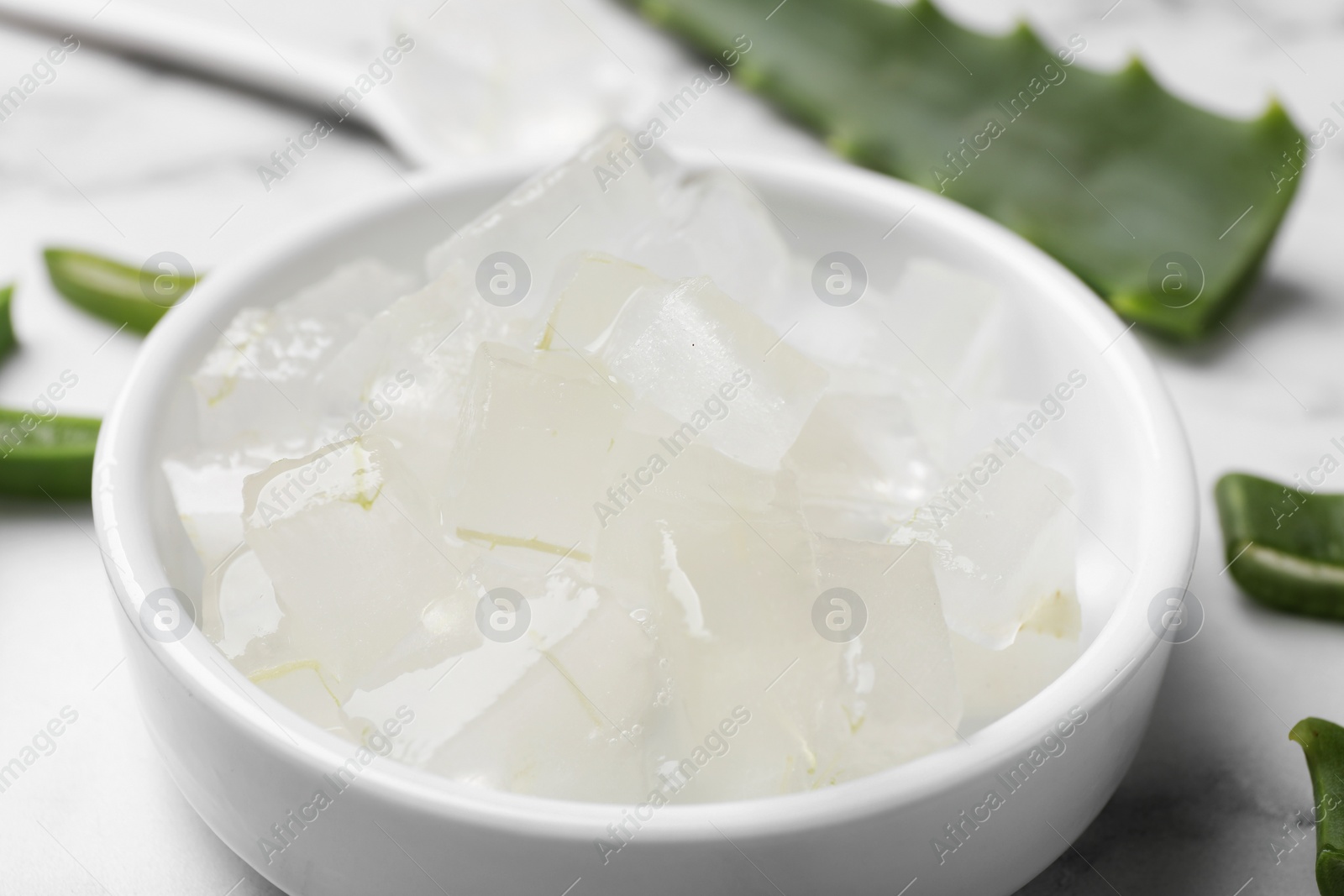 Photo of Aloe vera gel and slices of plant on white table, closeup