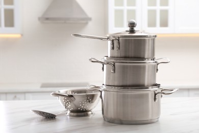 Set of stainless steel cookware and kitchen utensils on white table indoors