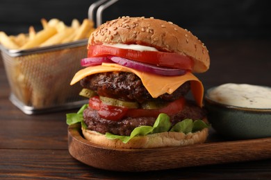 Tasty cheeseburger with patties, tomato and sauce on wooden table, closeup