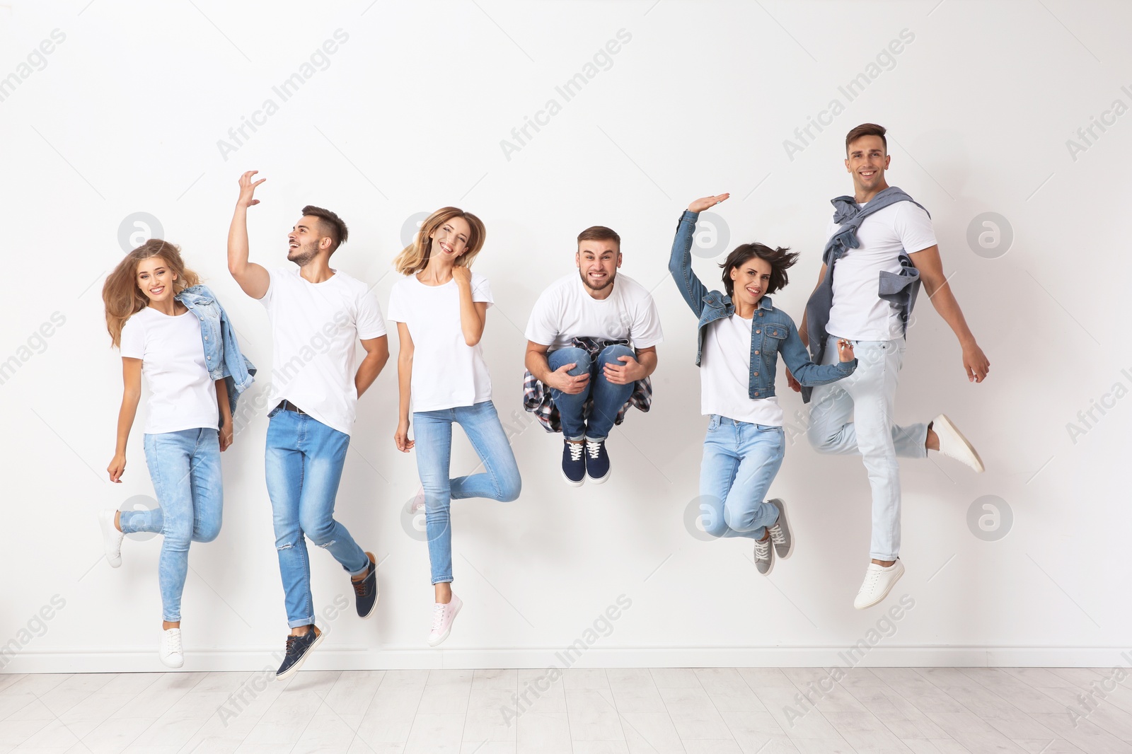 Photo of Group of young people in jeans jumping near light wall