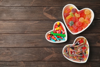Photo of Flat lay composition with different yummy candies in heart shaped bowls and space for text on wooden background