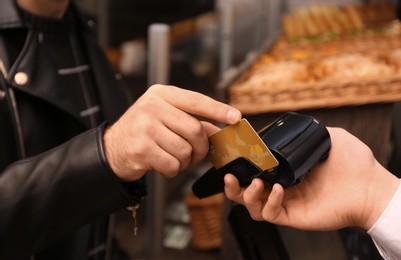 Photo of Man with credit card using payment terminal at shop, closeup