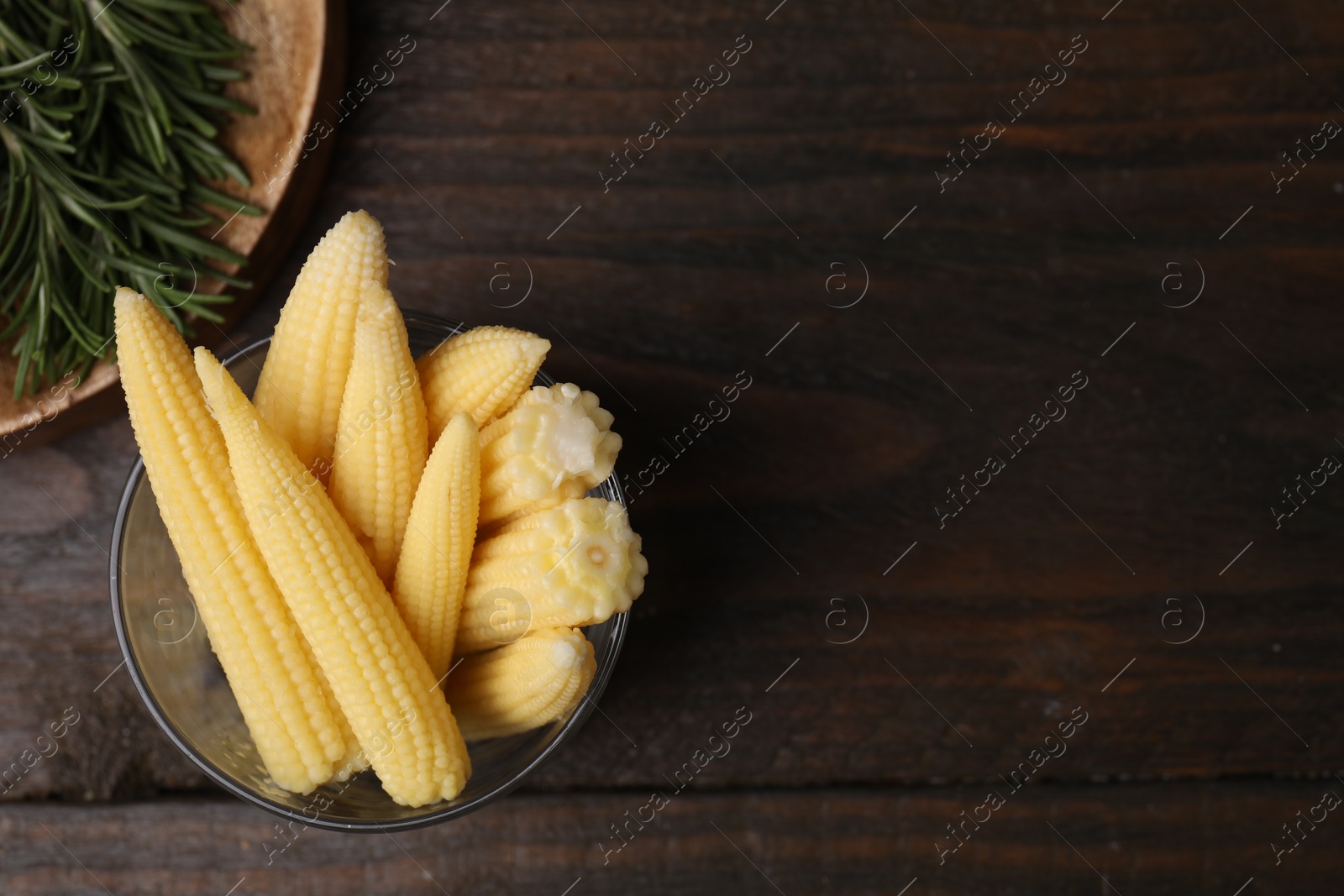 Photo of Tasty fresh yellow baby corns in glass on wooden table, top view. Space for text