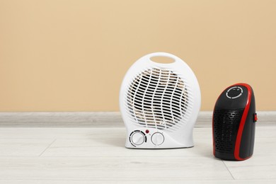 Photo of Modern electric compact and fan heaters on floor near beige wall, space for text