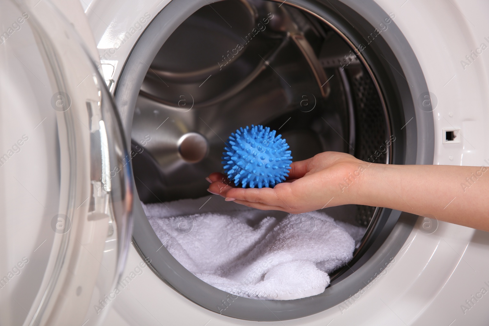 Photo of Woman putting blue dryer ball into washing machine, closeup