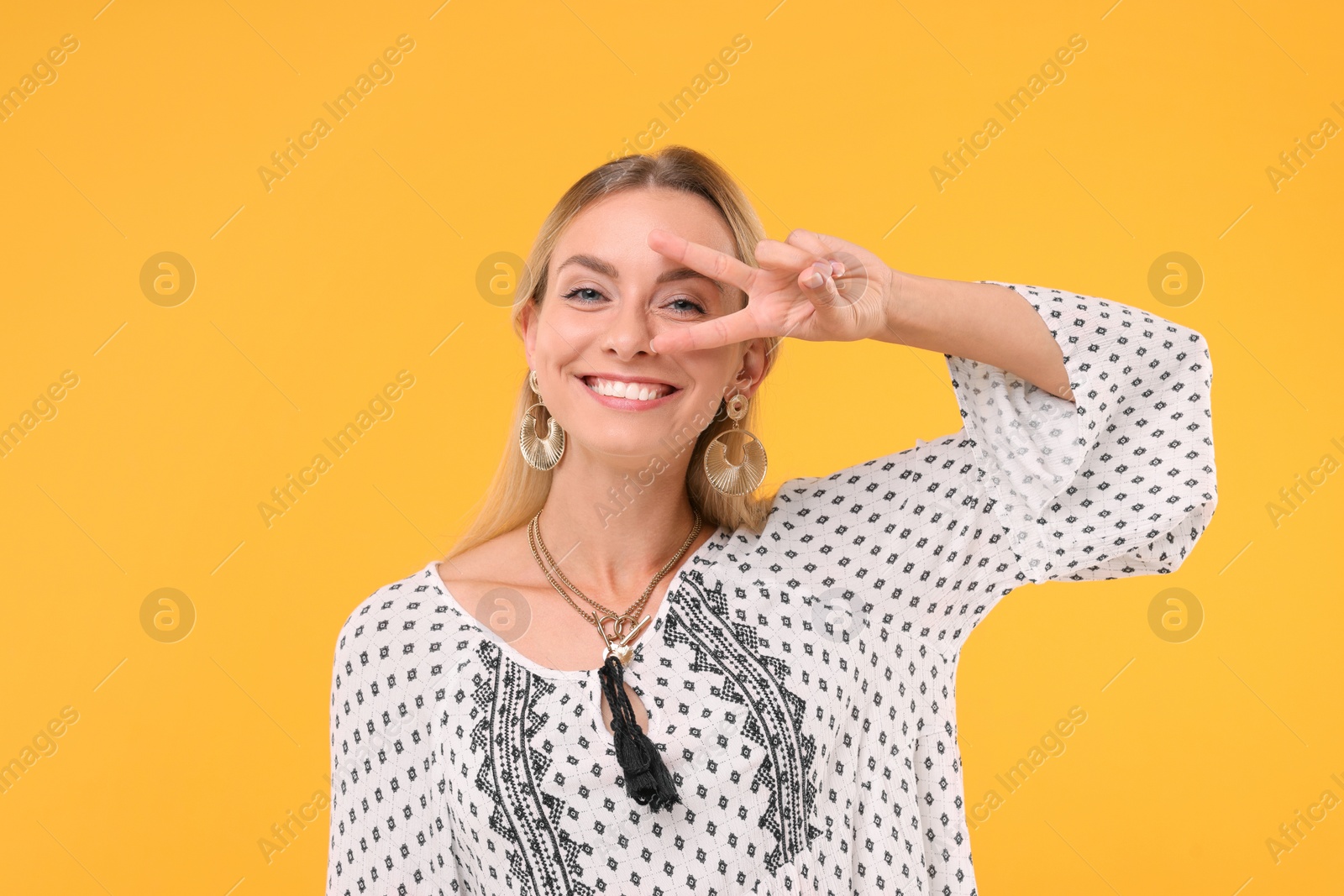 Photo of Portrait of smiling hippie woman showing peace sign on yellow background