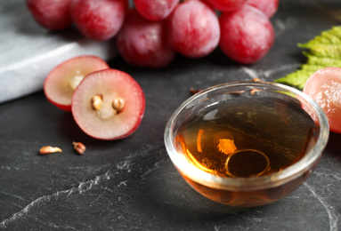 Photo of Bowl of natural grape seed oil on dark table. Organic cosmetic