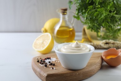 Photo of Tasty mayonnaise sauce in bowl, ingredients and spices on white table, closeup. Space for text