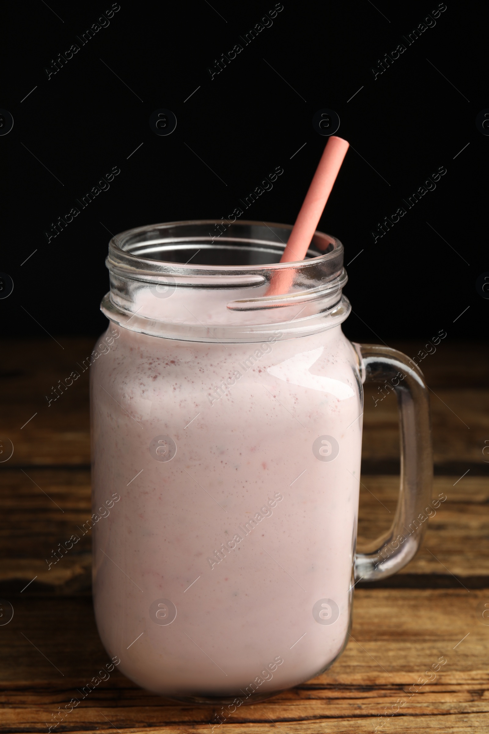 Photo of Tasty milk shake with straw in mason jar on wooden table