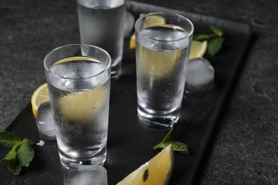 Photo of Shot glasses of vodka with lemon slices, mint and ice on grey table