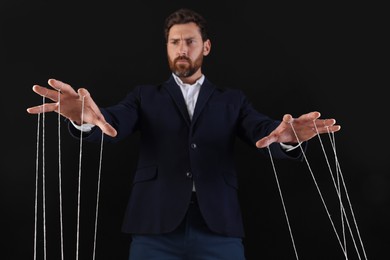 Photo of Man in suit pulling stringspuppet on black background, low angle view