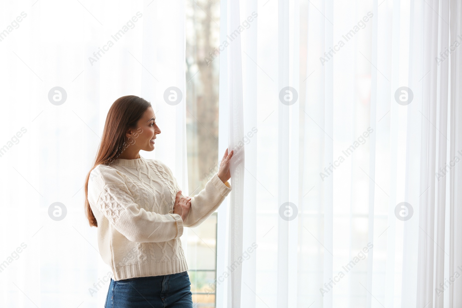 Photo of Young woman opening window curtains at home