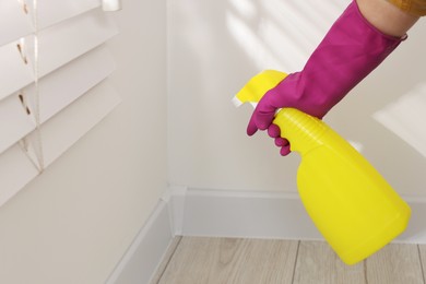 Photo of Woman in rubber glove with spray bottle near wall indoors, closeup
