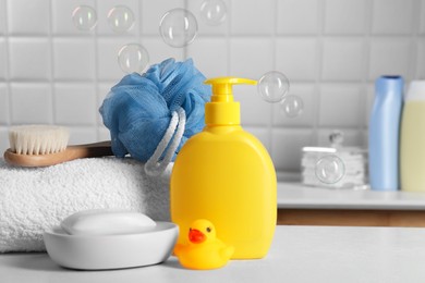 Photo of Baby cosmetic products, bath duck, brush and towel on white table against soap bubbles. Space for text