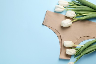 Beige women's underwear and tulips on light blue background, flat lay. Space for text