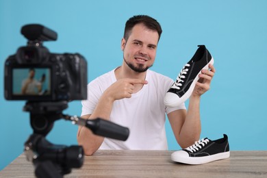 Smiling fashion blogger showing sneakers while recording video at table against light blue background