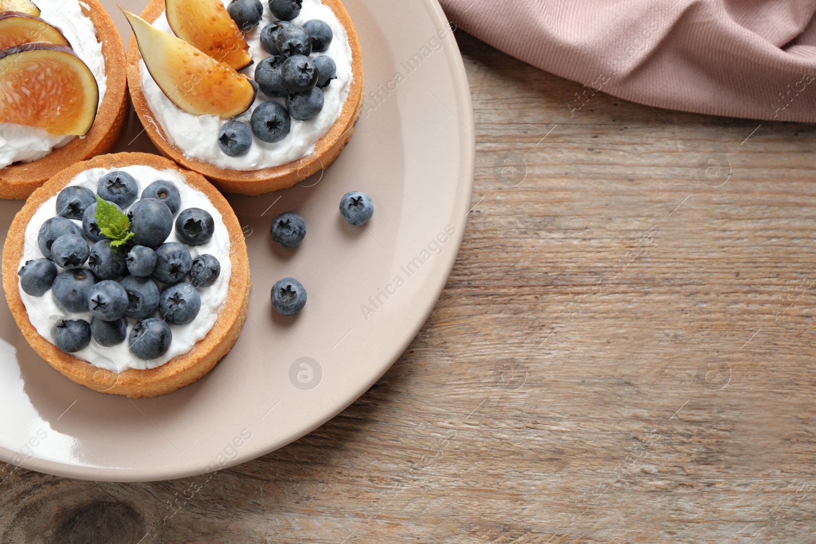 Photo of Tarts with blueberries and figs served on wooden table, top view with space for text. Delicious pastries