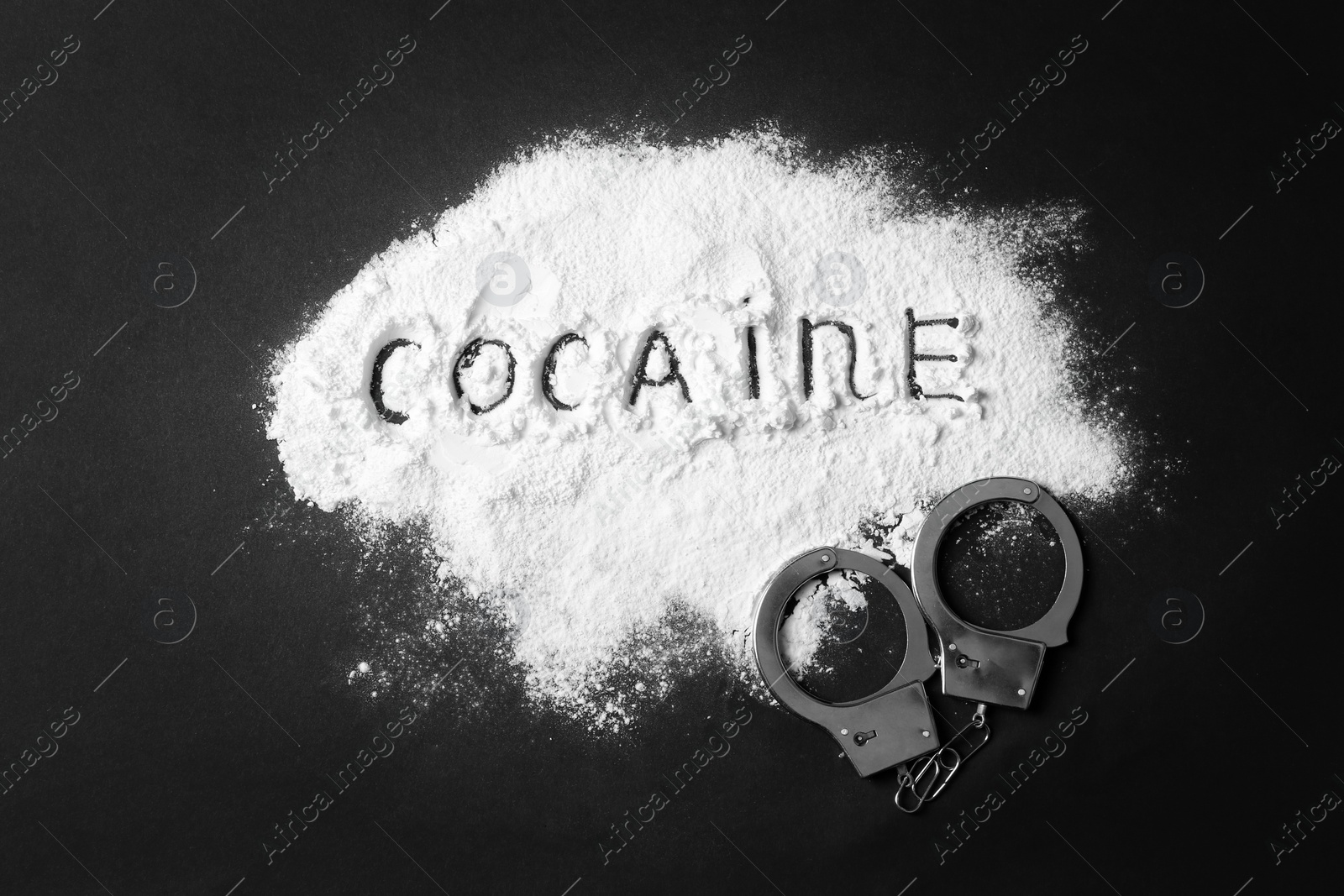 Photo of Heap of white powder with written word Cocaine and handcuffs on black background, top view