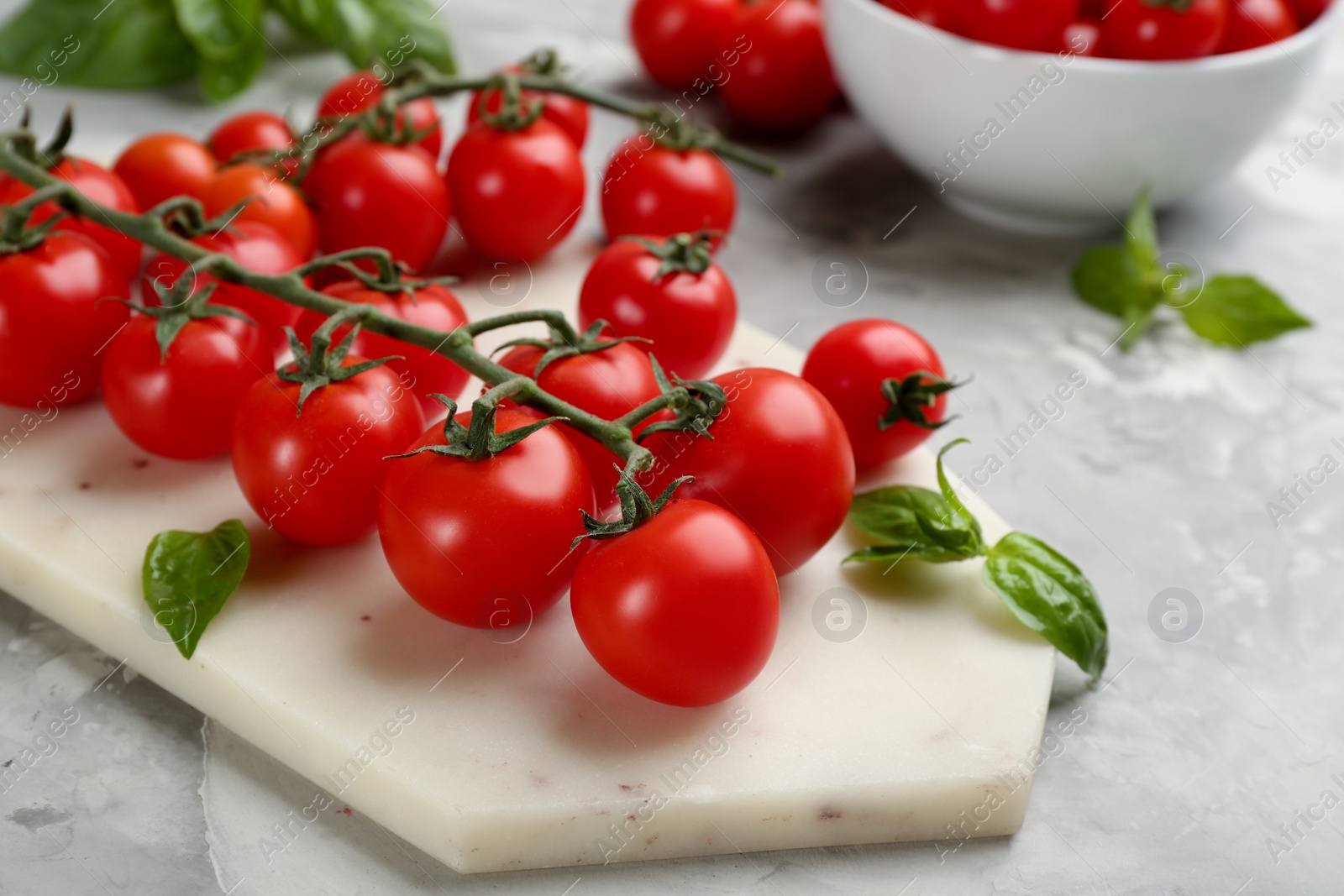 Photo of Fresh ripe cherry tomatoes and basil on light grey table, closeup