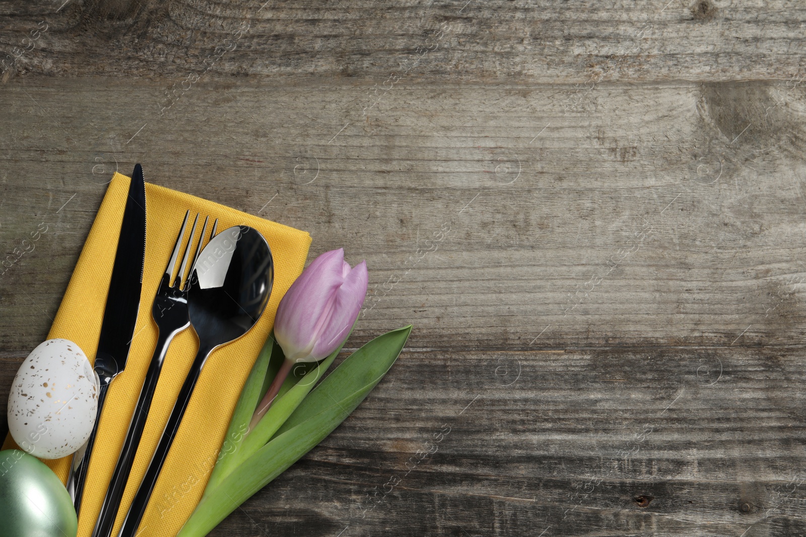 Photo of Cutlery set, painted eggs and beautiful flower on wooden table, flat lay with space for text. Easter celebration