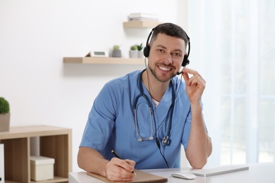 Photo of Doctor with headset sitting at desk in clinic. Health service hotline