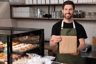 Photo of Happy seller with paper bag at cashier desk in bakery shop