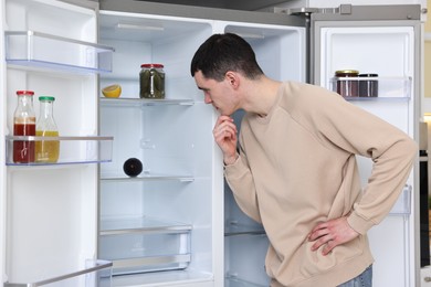 Photo of Thoughtful man near empty refrigerator in kitchen