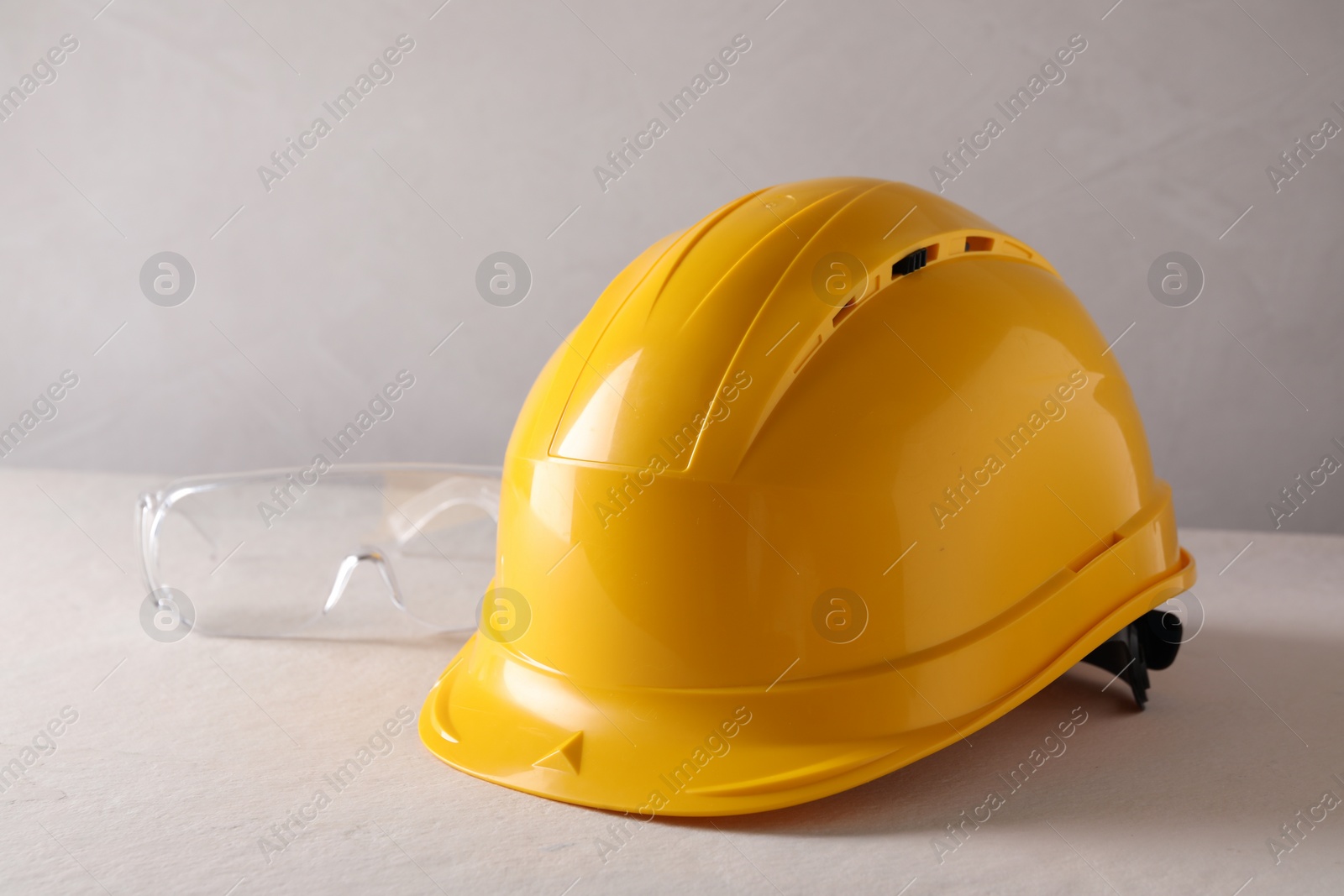 Photo of Hard hat and goggles on white table. Safety equipment