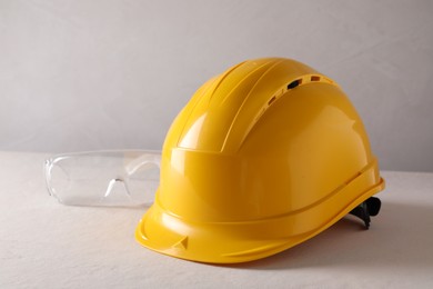 Hard hat and goggles on white table. Safety equipment